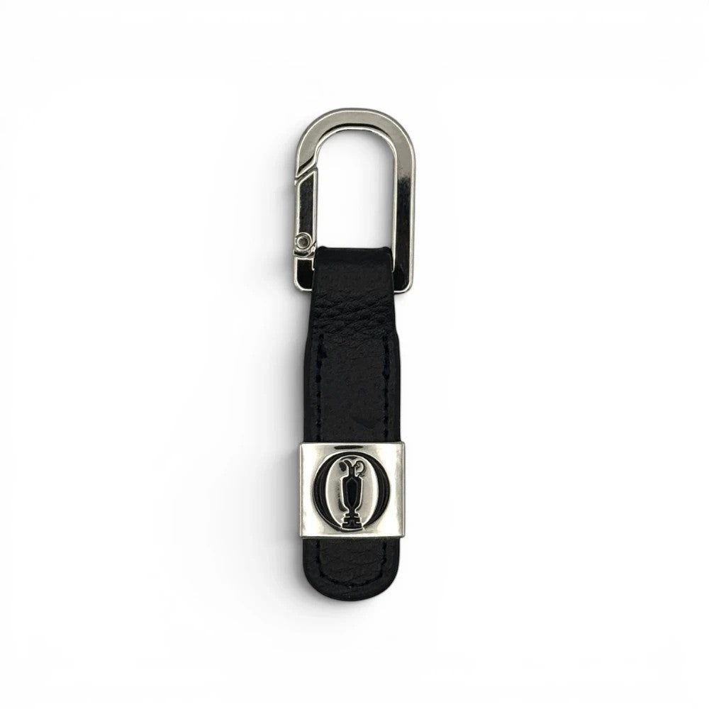 The Open Leder-Schlüsselanhänger in Schwarz mit silbernem Trophäen-Emblem und Karabinerhaken.
